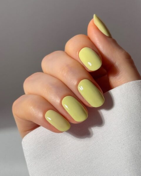 Zdjęcie dłoni ze średniej długości, owalne paznokcie w kolorze pistacjowej zieleni. Dłoń pozuje tak, by prezentować manicure.