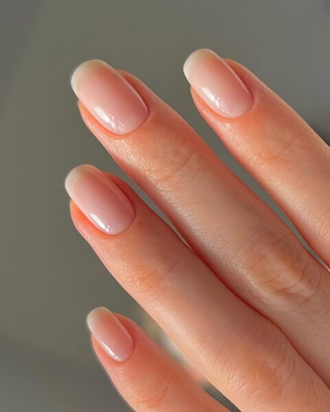 Zdjęcie dłoni ze zbliżeniem na skandynawski manicure: średniej długości kwadratowe paznokcie pomalowane półtransparentną odżywką.