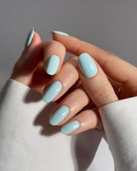 Zdjęcie dłoni ze zbliżeniem na manicure: średniej, owalne paznokcie skandynawskie w kolorze pastelowego błękitu. Dłonie pozują tak, by prezentować manicure.