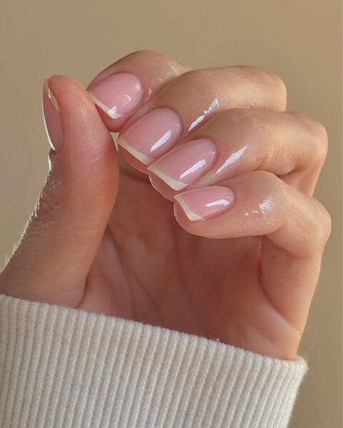 Zbliżenie na dłoń z klasycznym, schludnym manicure francuskim na krótkich, kwadratowych paznokciach, w ciepłym świetle. Skórki są wyraźnie nawilżone i zadbane, co podkreśla elegancję i jakość stylizacji.