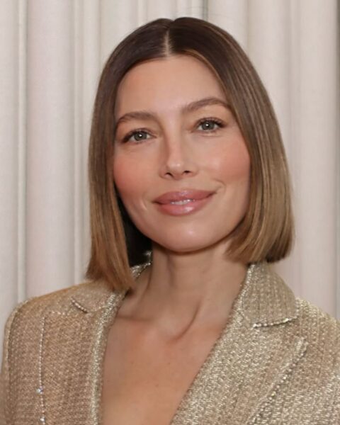 Portret Jessiki Biel w błyszczącej, złotej marynarce. Ma włosy w stylowym, prostym bobie i promienny, naturalny makijaż z ustami w kolorze nude z połyskiem i brzoskwiniowym różem. Zdjęcie inspiruje do poznania 5 trików w makijażu, które odejmują lat.