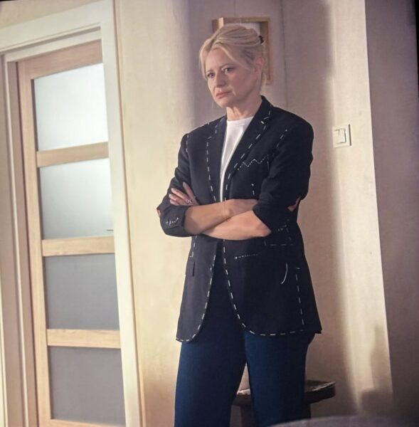 Kobieta w blond włosach i w granatowej marynarce oraz granatowych jeansach. 