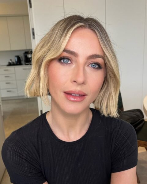 Zbliżenie na twarz aktorki i tancerki Jules Hough w naturalnym, dziennym świetle, podkreślające jej niebieskie oczy i nowoczesną fryzurę typu bob. Makijaż jest subtelny, bazujący na świeżej, rozświetlonej cerze i delikatnym konturowaniu. Uwagę zwracają pięknie wytuszowane rzęsy i błyszczący, nude'owy błyszczyk na ustach. Jules ma na sobie czarną, prostą koszulkę, a jej stylizacja emanuje niewymuszonym szykiem.