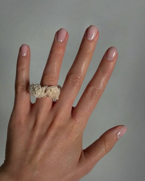 Perfekcyjny manicure nude w odcieniu delikatnego różu, podkreślający naturalne piękno i zadbane dłonie. Krótka, owalna płytka to kwintesencja klasycznej elegancji i stylu quiet luxury w urodzie. Uwagę zwraca także oryginalny, rzeźbiony pierścionek w kolorze écru na palcu serdecznym, będący inspiracją dla kobiet, które łączą minimalizm z artystycznym detalem.