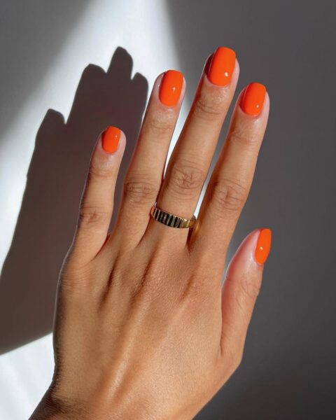 Energetyczny pomarańczowy manicure idealny na wczesną jesień lub lato. Krótkie paznokcie o owalnym/zaokrąglonym kształcie pomalowane błyszczącym, nasyconym lakierem w odcieniu intensywnej pomarańczy (mandarynka, dynia). Żywy kolor świetnie komponuje się z opaloną skórą i jest modną, odważną propozycją dla kobiet, które lubią kolorystyczne akcenty w stylizacji.