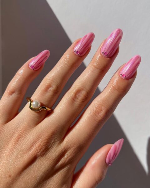 Manicure w klimacie lat 2000. – długie paznokcie w kształcie migdała pomalowane intensywnie różowym, perłowym (chromowym) lakierem. Paznokcie mają delikatną teksturę, wyglądającą jak muszla. U nasady każdego paznokcia umieszczono kilka drobnych, różowych cyrkonii. Dłoń zdobi złoty pierścionek z białą perełką.