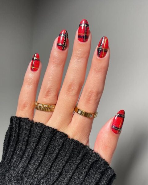 Uwagę skupia dłoń w czarnym, dzianinowym swetrze, ozdobiona złotą biżuterią (dwa pierścionki, w tym jeden Cartier Love), z eleganckim, świątecznym manicurem w kratkę (tartan). Paznokcie w kształcie migdała, wszystkie pomalowane w wyrazisty wzór czerwono-czarnej kraty (szkockiej), akcentowany złotymi, cienkimi liniami. Stylizacja idealna na Boże Narodzenie lub zimowy sezon.