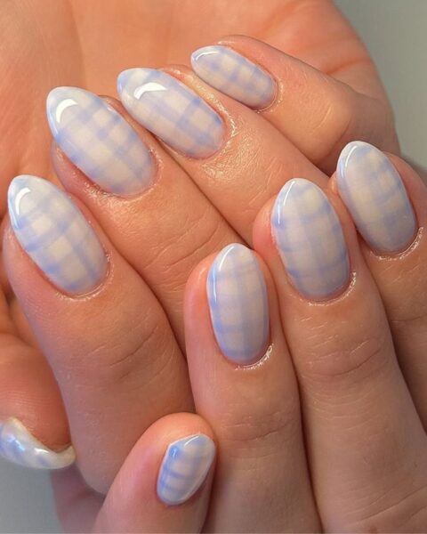 Delikatny, eteryczny manicure w kratkę na długich, owalnych paznokciach. Wszystkie paznokcie pokrywa subtelny wzór kraty stworzony z cienkich, jasnoniebieskich i białych linii na mlecznej, przezroczystej bazie. Efekt przypomina "mgiełkę" lub akwarelę. Manicure jest lśniący, idealny dla kobiet ceniących subtelne i eleganckie wzory.