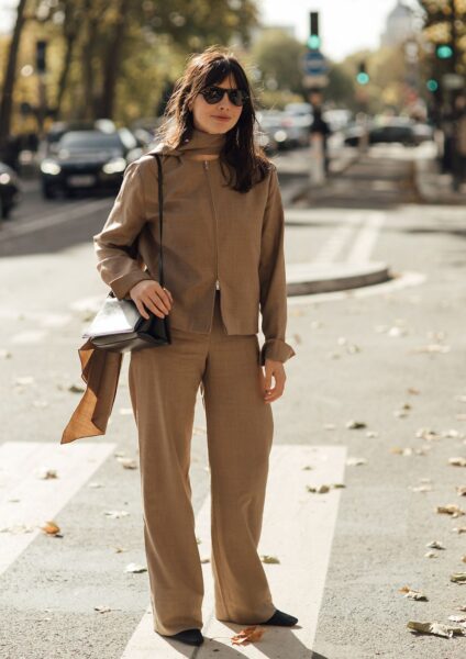 Stylowa kobieta w beżowym, monochromatycznym garniturze z szerokimi spodniami i kurtką z zamkiem błyskawicznym oraz szalem w tym samym kolorze. Street style z Paryża, idealny przykład eleganckiego, minimalistycznego i modnego zestawu na jesień. Czarne okulary przeciwsłoneczne i klasyczna czarna torebka dopełniają look.